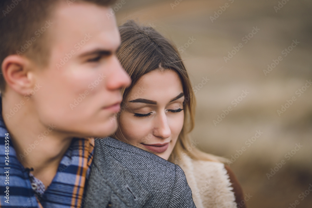 A nice beautiful lovely couple in the park or field. man in Gray coat and scarf with girl woman in brown coat. lovers walking hold hands. put her head on his shoulder hugged behind A nice beautiful lovely couple in the park or field. man in Gray coat and scarf with girl woman in brown coat. lovers walking hold hands. put her head on his shoulder hugged behind