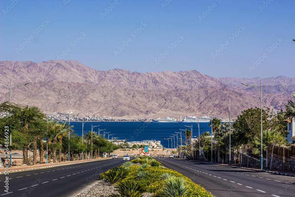south Middle East city view park outdoor district car road down to Gulf of Aqaba Red sea bay, palm trees alley way, bare desert mountain ridge horizon background in Jordan Arabian country 