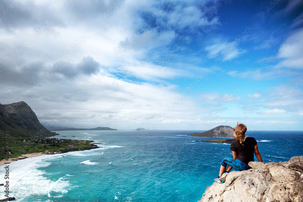 Woman sitting atop a cliff overlooking Oahu, Hawaii's south shore
