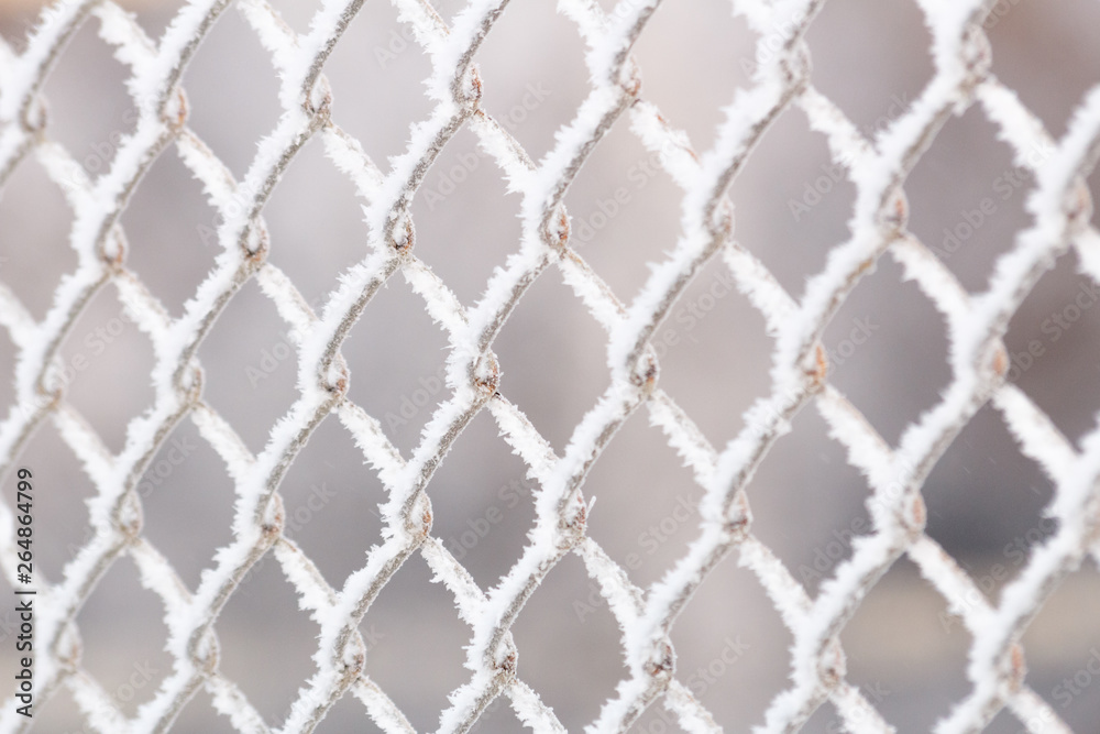 Naklejka premium Abstract background of wire fence in winter, covered with frozen snow and ice. Shallow depth of field, blurred background