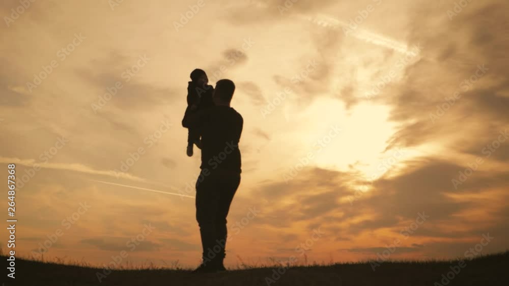 Silhouettes father and little son playing on the meadow at the sunset time. Concept of friendly family. Silhouettes father and little son playing on the meadow at the sunset time. Concept of friendly family.