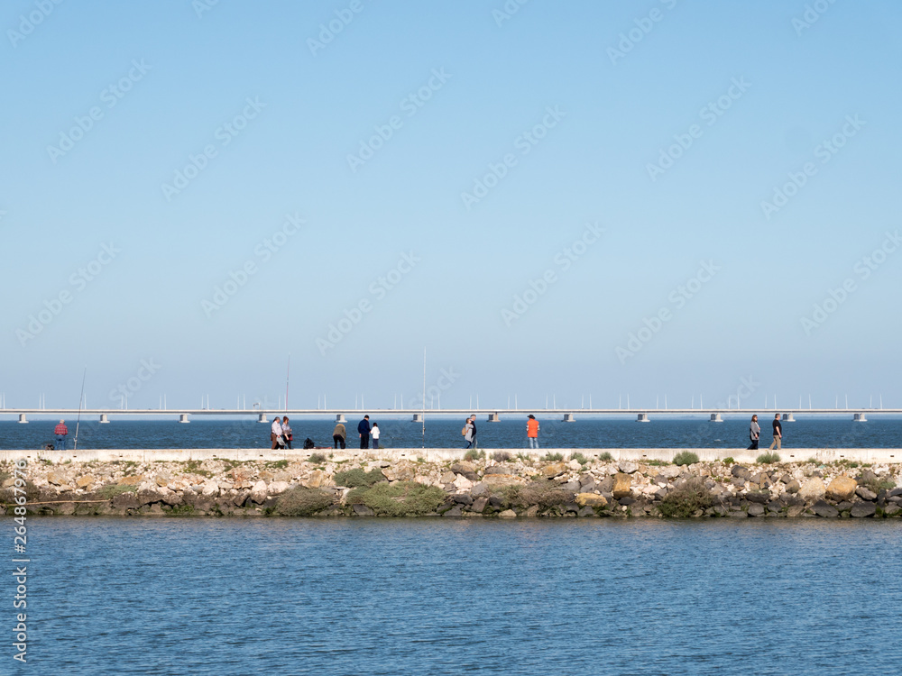 People wakling on a seafront parapet and looking to a sea and water