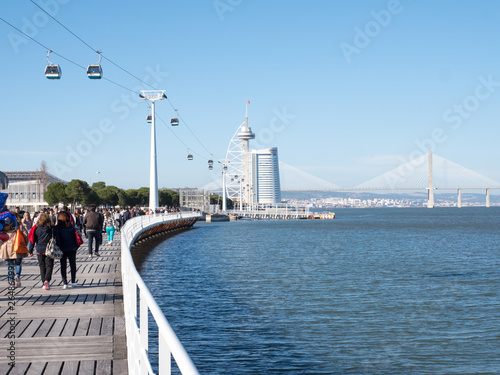 People wakling on a seafront parapet and looking to a sea and bridge in Lisbon