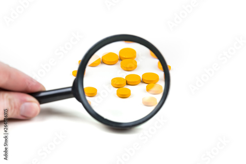 Hand holding a black magnifying glass looking at pills