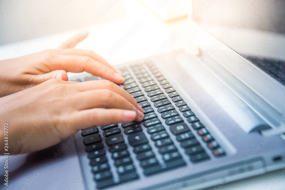 Closeup top view woman's hands typing on a laptop computer keyboard on a white desk with sun flare lighting effect. Closeup top view woman's hands typing on a laptop computer keyboard on a white desk with sun flare lighting effect.