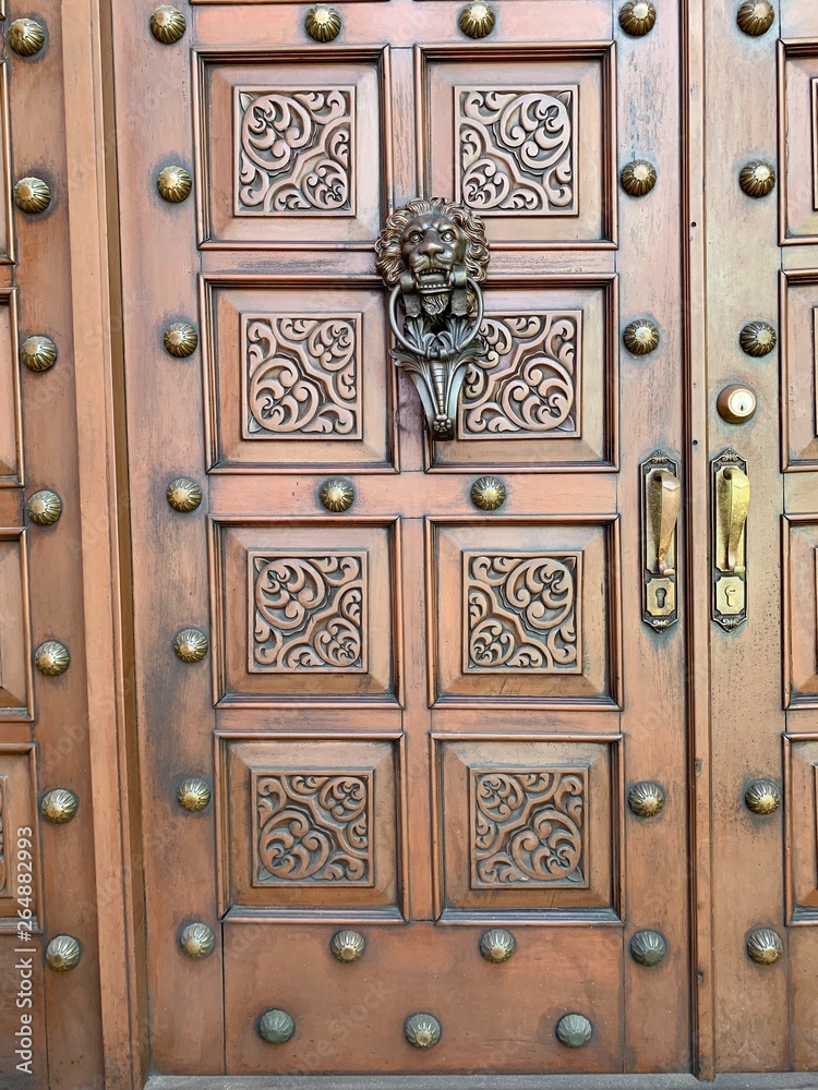 Puerta de madera en cedro, con adornos de bronce y picaporte con figura de León. Puerta de madera en cedro, con adornos de bronce y picaporte con figura de León.