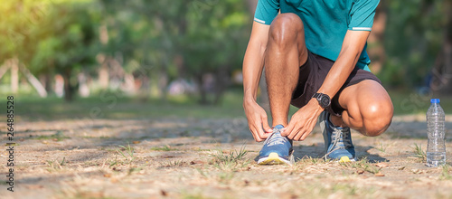 Young athlete man tying running shoes in the park outdoor, male runner ready for jogging on the road outside, asian Fitness walking and exercise on forest trail in morning. wellness and sport concepts photo