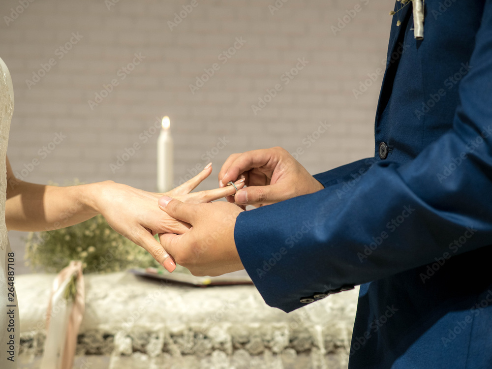 Groom puts wedding ring on bride's finger in wedding ceremony.