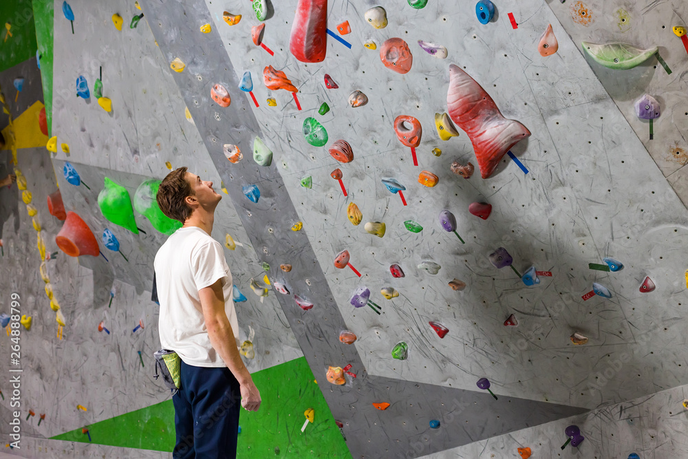 Rock climber stands and looks at the climbing wall with hooks in the boulder hall