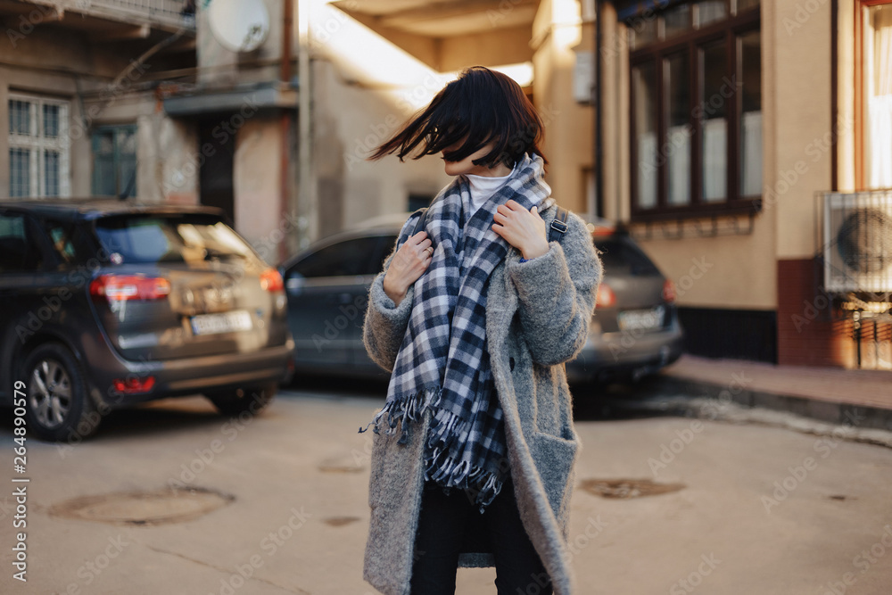 Attractive positive young girl wearing glasses in a coat on the background of buildings on cars