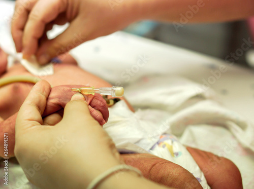 The nurse hands is stabbed injection plug at sick newborn baby's hand to prepare fill the saline solution and medicine.