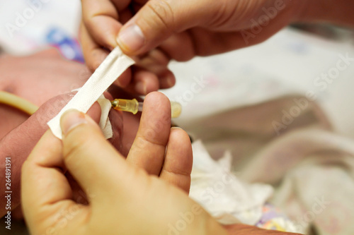 Nurse hands using medical adhesive plaster stick and wrap safely on IV Catheter and sick newborn baby's hand  for prepare fill the saline solution and medicine.