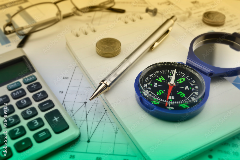 Blue compass, pen, coin, notebook, calculator, glasses on financial graph, Business investment concept Blue compass, pen, coin, notebook, calculator, glasses on financial graph, Business investment concept