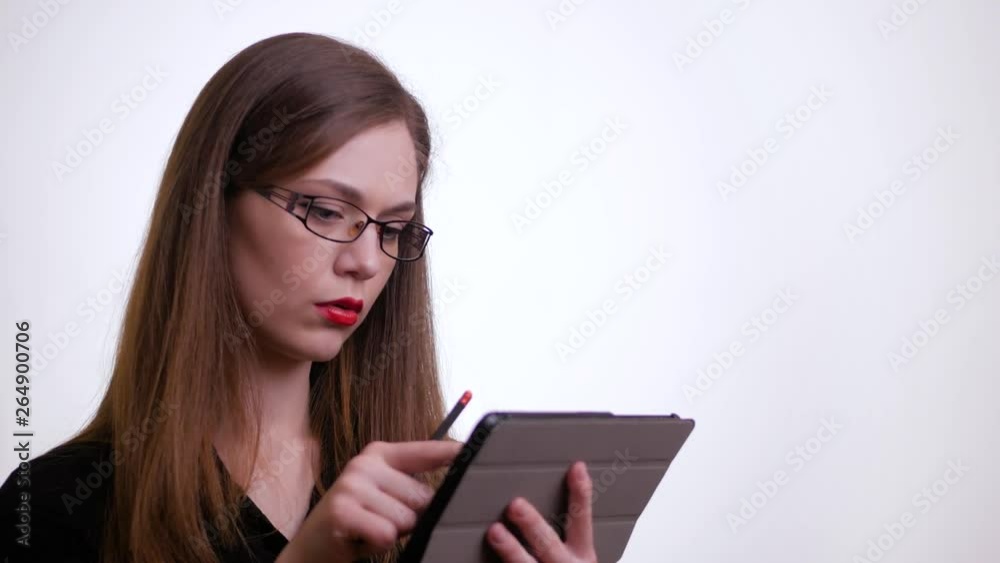Serious caucasian young woman in stylish eyeglasses using internet on tablet. Office lady in a black shirt and tablet device. White isolated background. Serious caucasian young woman in stylish eyeglasses using internet on tablet. Office lady in a black shirt and tablet device. White isolated background.