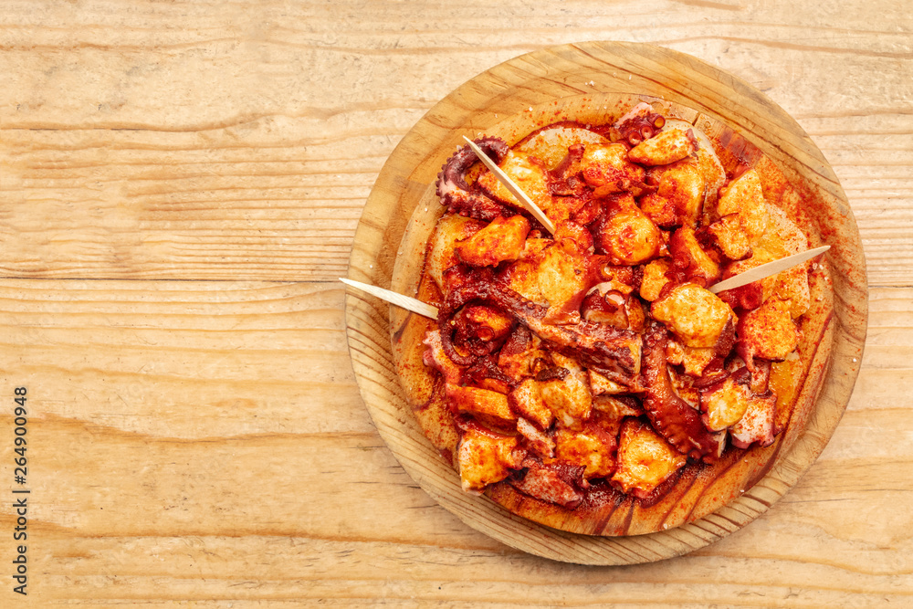 Pulpo a la gallega, an octopus with boiled potatoes and paprika, typical Spanish Galician dish, on a traditional wooden plate, shot from above on a wooden background with a place for text Pulpo a la gallega, an octopus with boiled potatoes and paprika, typical Spanish Galician dish, on a traditional wooden plate, shot from above on a wooden background with a place for text