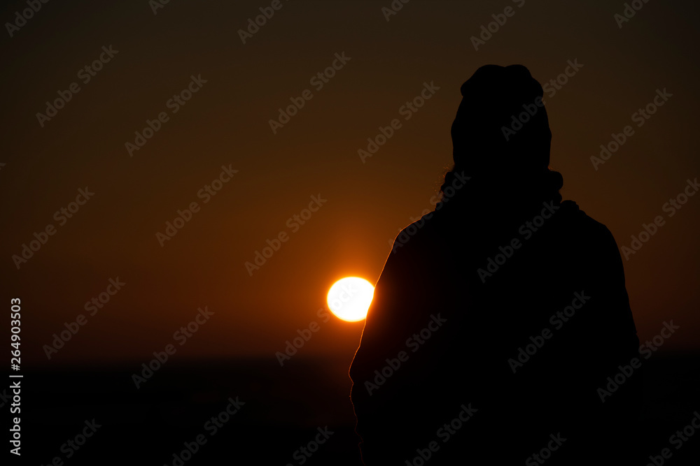 The dark silhouette of a young girl dreaming against the stunning sunset.
