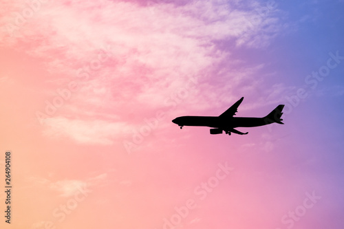 Silhouette an airplane in flight against rainbow colorful sky and clouds. Abstract pastel beautiful landscape at sunset.