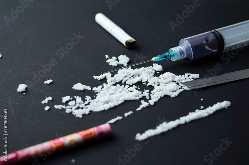 Cocaine and Indonesia rupiah ready for uses on dark table. Selective focus on syringe