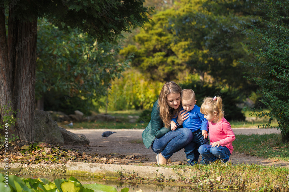 mother plays with her daughter and son in the park by the pond