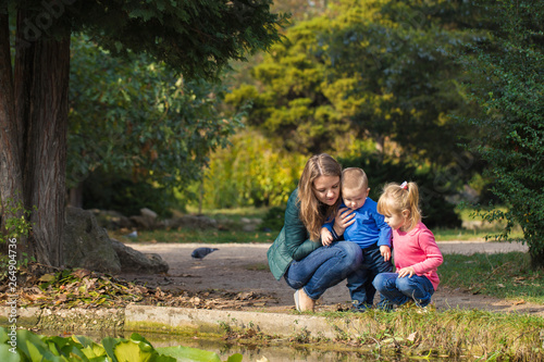 mother plays with her daughter and son in the park by the pond