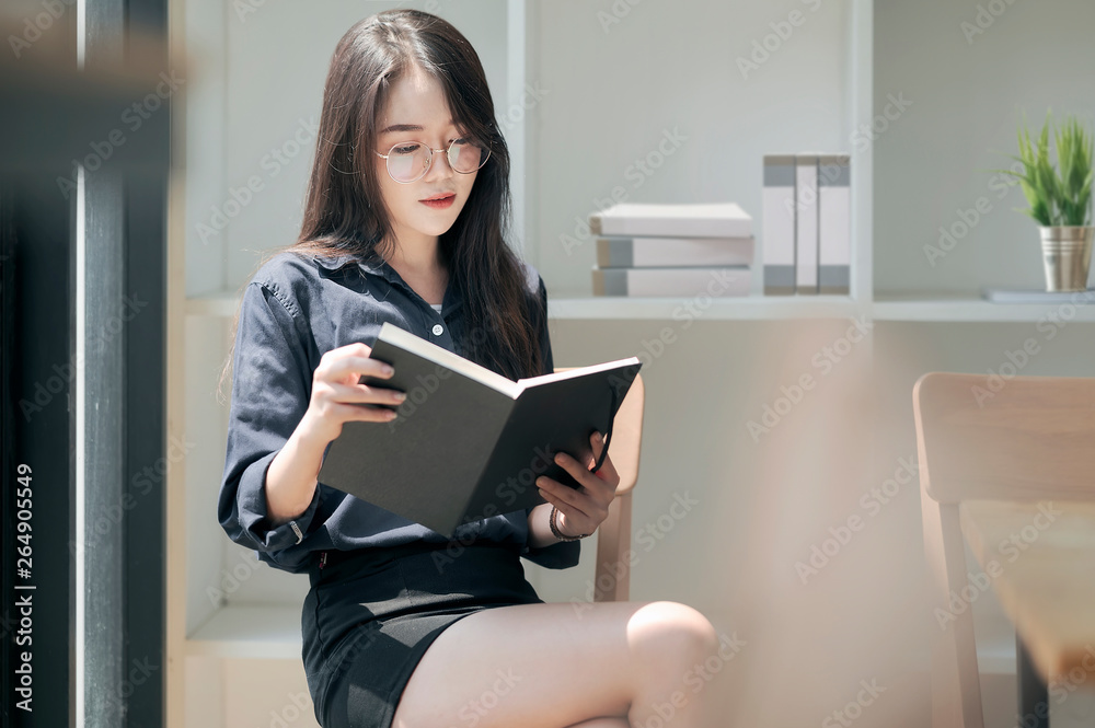 Young asian woman reading a book while sitting near window in white room. Young asian woman reading a book while sitting near window in white room.
