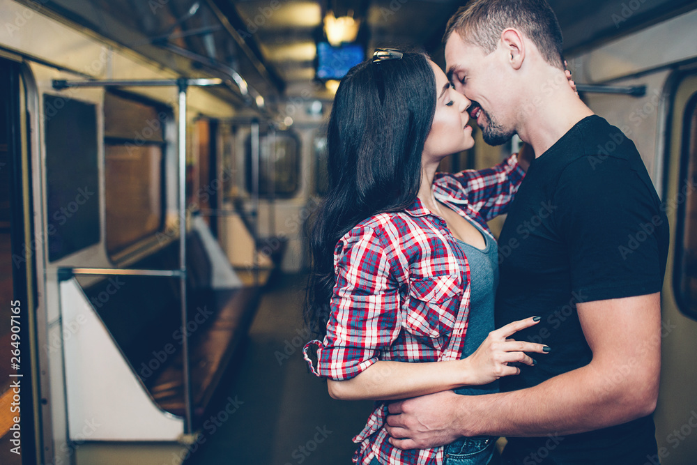 Young man and woman use underground. Couple in subway. Romantic kiss. Alone together in carriage. Tender picture. Standing in middle of subway carriage.