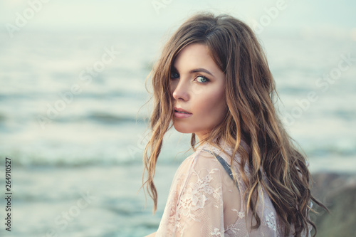 Beautiful woman face. Perfect model girl with long curly hair on ocean background, romantic portrait