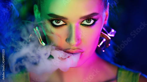 Fototapeta Naklejka Na Ścianę i Meble -  Fashion girl smoking e-cigarette in neon lights