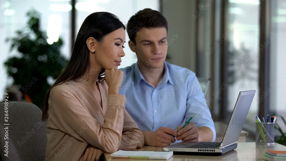 Male and female colleagues looking laptop in office, working at project together Male and female colleagues looking laptop in office, working at project together