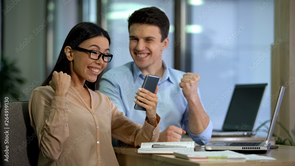 Fototapeta premium Male and female showing success gesture holding smartphone, startup application