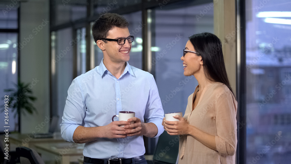 Smiling man and woman talking during break holding coffee cups, colleagues
