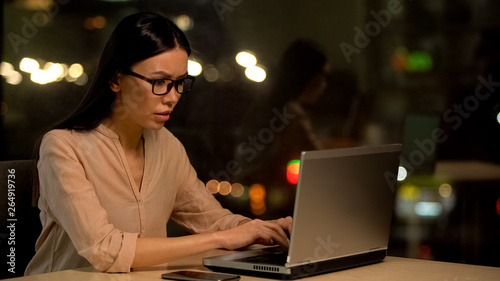 Concentrated female in eyeglasses working laptop, preparing report, project