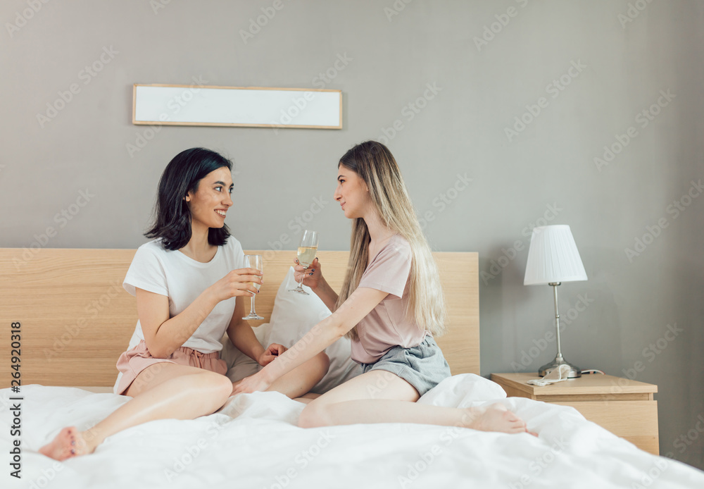 two awesome girls celebrating an event in the modern bedroom. close up photo. party at home.celeation, Birthday.two best friends with glasses sitting on the bed and having a conversation. two awesome girls celebrating an event in the modern bedroom. close up photo. party at home.celeation, Birthday.two best friends with glasses sitting on the bed and having a conversation.