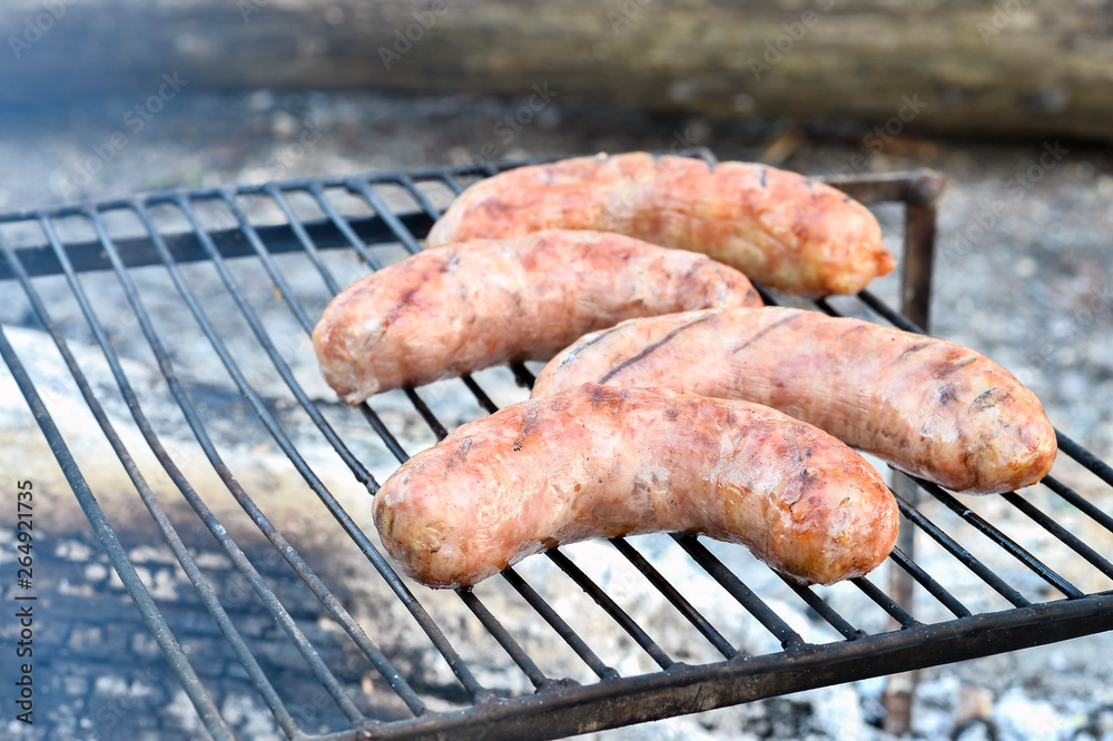 Pork sausages are roasted on the coals on the grill.