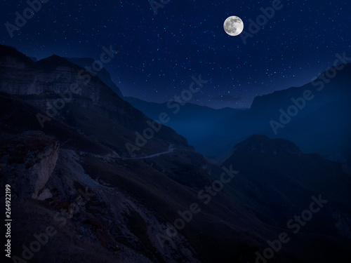 Mountain Road through the forest on a full moon night. Scenic night landscape of country road at night with large moon. Long shutter photo