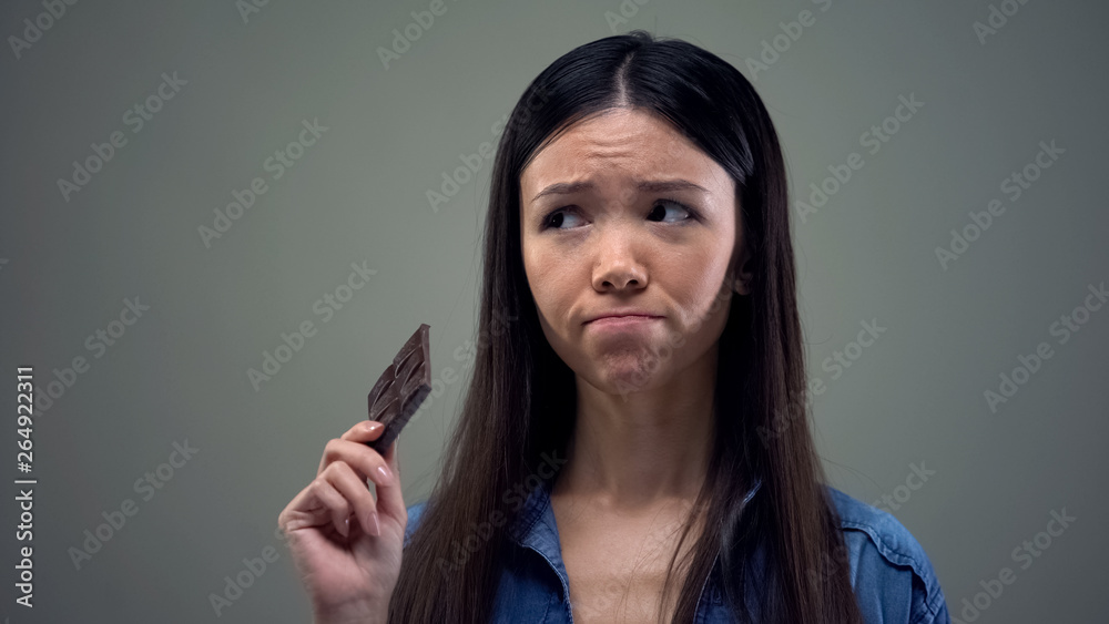 Fototapeta premium Sad asian girl dreaming about sweet chocolate keeping diet, healthy nutrition