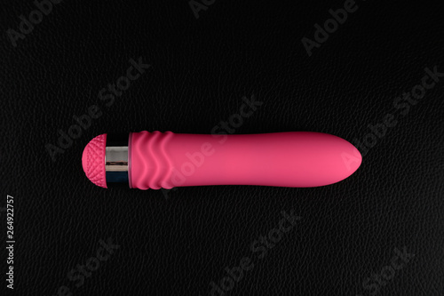 Pink dildo on black skin. Dark background. Artistic lighting.