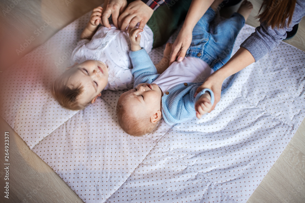 Two happy smiling male infant twins lying on blanket being fondled by parents hands