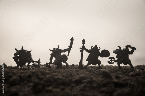 Medieval battle scene with cavalry and infantry. Silhouettes of figures as separate objects  fight between warriors on sunset foggy background. Selective focus
