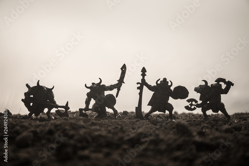 Medieval battle scene with cavalry and infantry. Silhouettes of figures as separate objects, fight between warriors on sunset foggy background. Selective focus