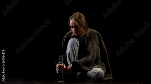 Miserable alcoholic female sitting in darkness with bottle of vodka, addiction