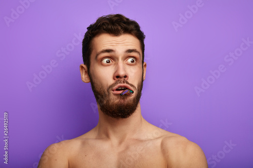 scared bug-eyed man with toothbrush looking aside, expressing shock and full disbelief. close up portrait. isolated over blue background