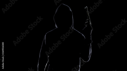 Silhouette of serial killer in hoodie threatening with gun, preparing to murder