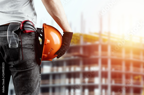 A builder, an architect holds in his hand a construction helmet against the background of a construction site, a tape measure. Concept architecture, construction, engineering, design, repair.