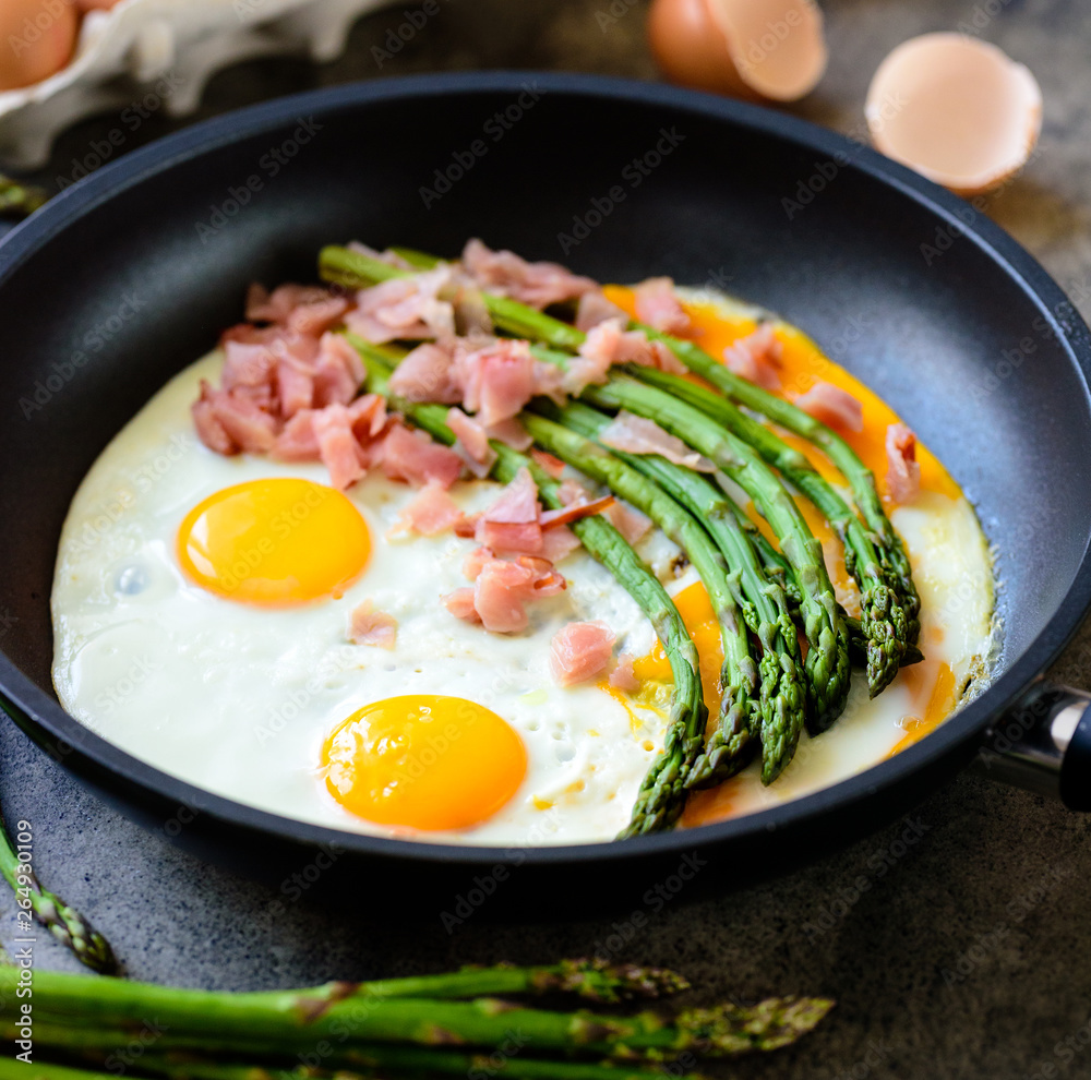 Fried eggs with asparagus and ham on a dark stone board