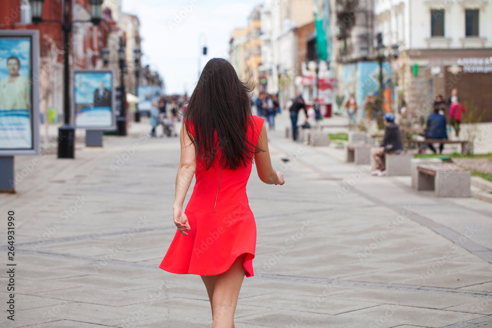 Young beautiful woman in red dress walking in summer street