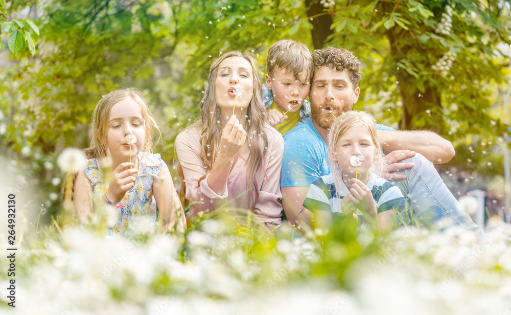 Family of five sitting on a meadow blowing dandelion flowers Family of five sitting on a meadow blowing dandelion flowers