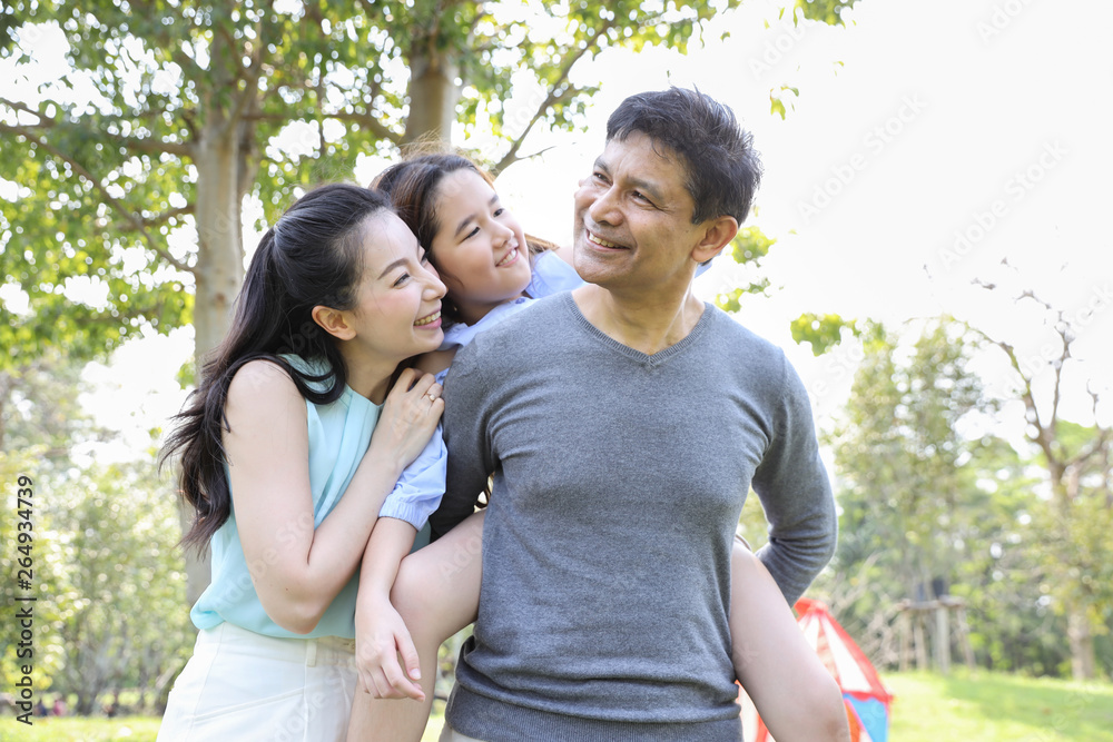 image of happy family, daughter riding behind father while parents smiling during summer time in the park image of happy family, daughter riding behind father while parents smiling during summer time in the park