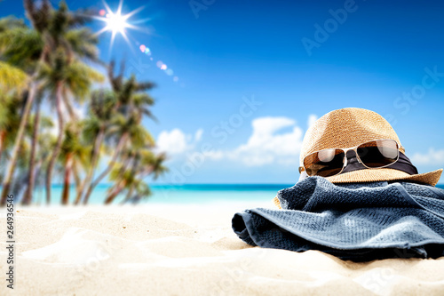 Summer sunglasses with hat on sand and blue towel. Free space for your decoration. Blurred background of beach with palms and ocean  © magdal3na