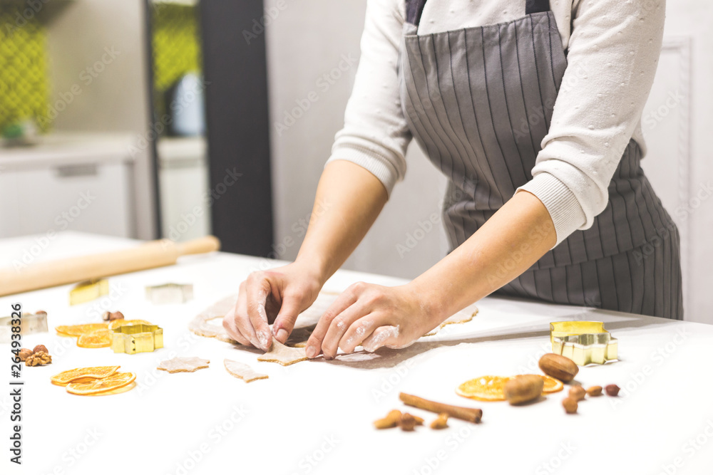 Young pretty woman prepares the dough and bakes gingerbread and cookies in the kitchen. She makes a star shape on the dough. Merry Christmas and Happy New Year.